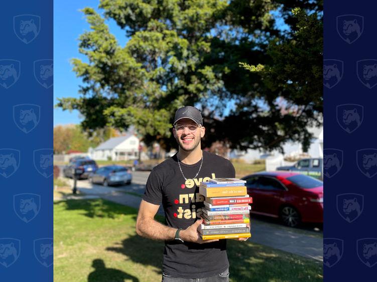 Man holding stack of books in front of a tree